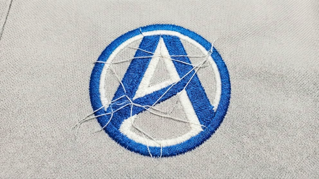 Messy embroidery logo on white fabric with visible jump stitches and loose threads