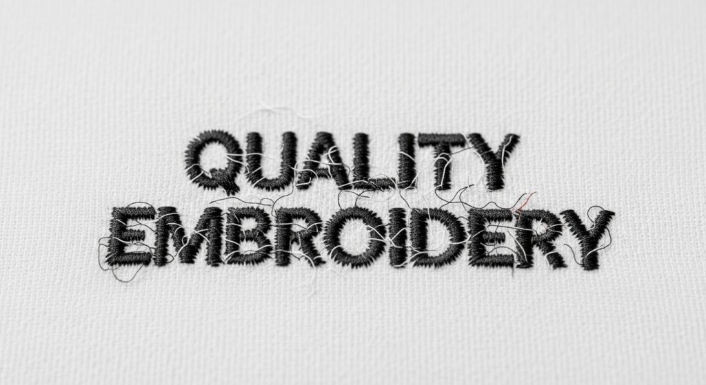 Close-up of poorly digitized small embroidery letters showing overlapping stitches, filled centers, and illegible text on white fabric