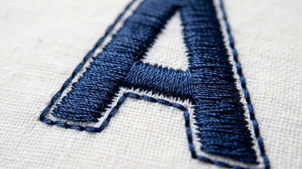close-up of running stitch tracing edge of embroidered letter A on white fabric