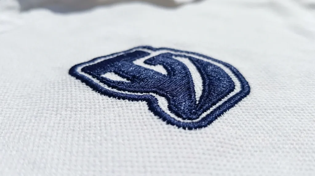 Satin stitch border outline applied over fill stitch edge on white polo embroidery to create clean sharp logo boundary